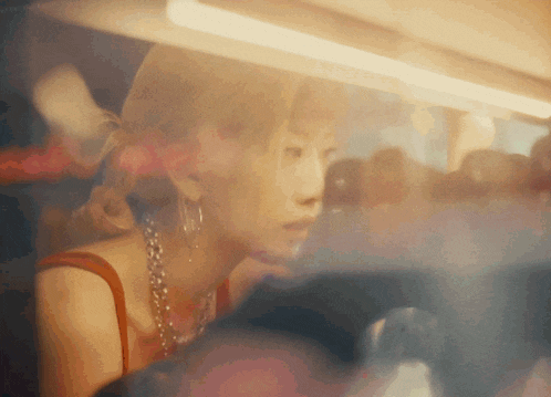 a woman wearing a red tank top and hoop earrings looks out a window
