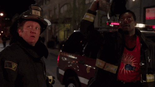 two firefighters one wearing a shirt that says little big heroes stand next to each other