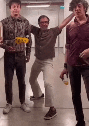 three men are standing next to each other in a hallway . one of them is holding a guitar .