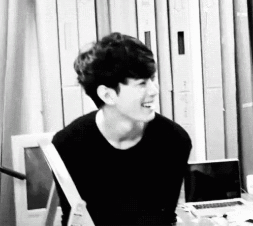 a black and white photo of a young man sitting at a table with a laptop .
