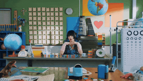 a girl sits at a desk with a globe and a heart on the wall