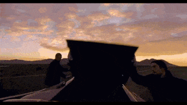 two men are standing next to a car at sunset