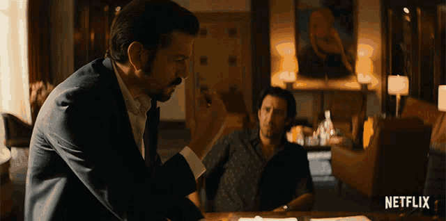 two men sitting at a table with a netflix logo on the bottom