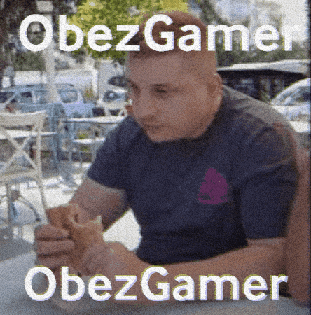 a man is sitting at a table eating a sandwich with the words obezgamer on the bottom right