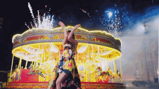 a woman is standing on a merry go round with fireworks behind her
