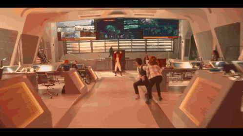 a couple of people are dancing in a room with a large screen behind them that says ' emergency '