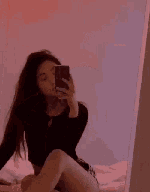 a woman is sitting on a bed taking a selfie with her phone .