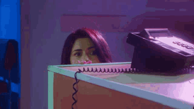 a woman is peeking out from behind a desk next to a telephone .