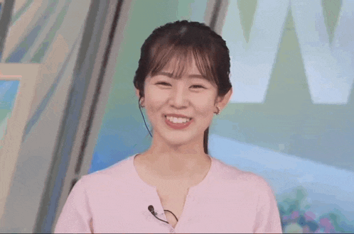 a woman in a pink shirt with a microphone on her neck smiles for the camera .