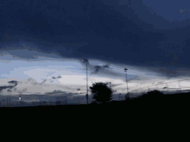 a dark blue sky with a few clouds and a few trees in the foreground