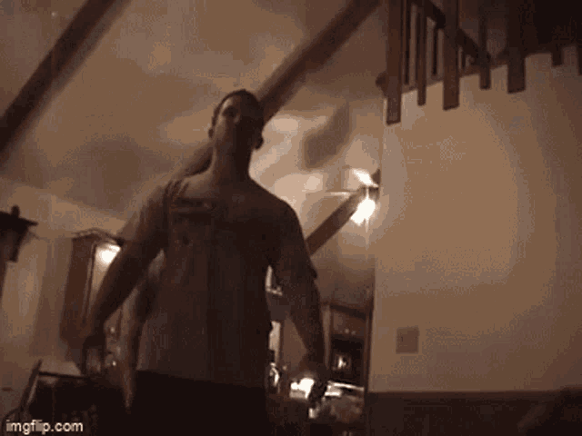 a man in a superman shirt is standing in a dark room with a staircase in the background