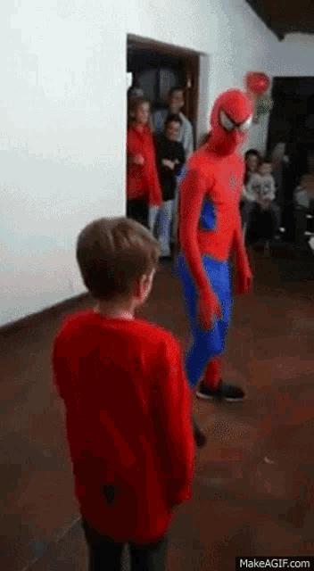 a boy in a red shirt is standing in front of a spiderman costume .