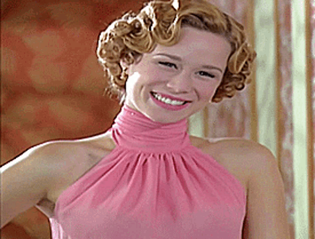 a woman in a pink dress is smiling and wearing curly hair