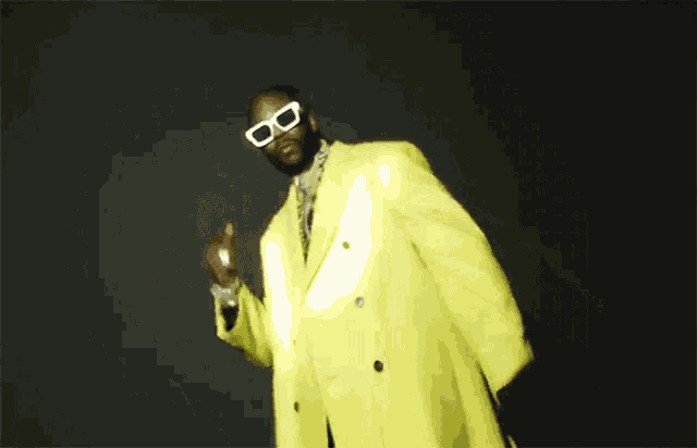 a man in a yellow suit and sunglasses is dancing .
