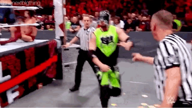 a wrestler in a green outfit is standing in front of a referee .