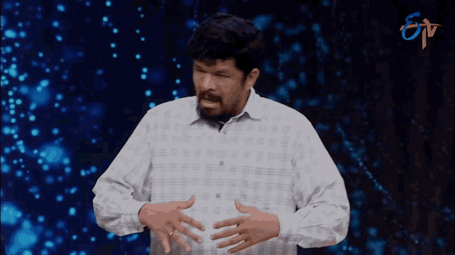 a man in a plaid shirt holds his hands on his stomach in front of a tv screen