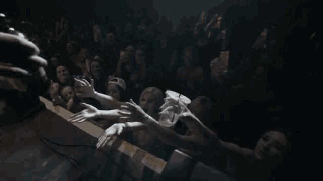 a crowd of people reaching out towards a microphone