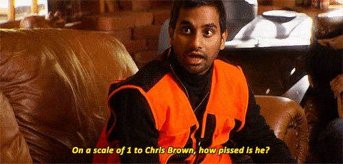 a man in an orange vest is sitting on a couch and talking to chris brown