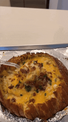 a bread bowl with cheese and bacon is being scooped out with a fork