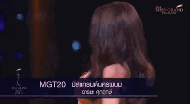 a woman in a strapless orange dress is smiling on a stage at miss grand thailand .