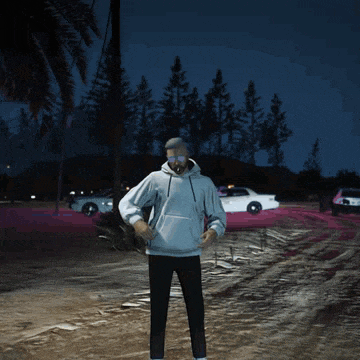 a man in a white hoodie stands in front of a burning vehicle