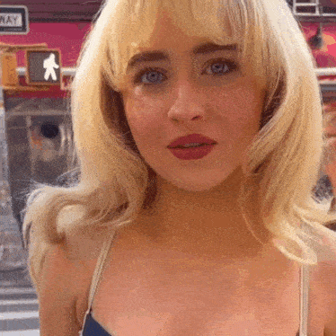 a woman with blonde hair and blue eyes is standing in front of a crosswalk sign .