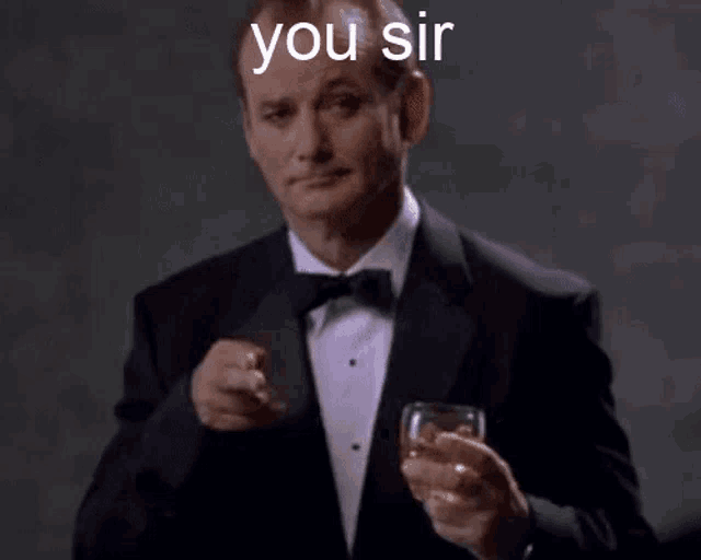 a man in a tuxedo is holding a glass of wine and making a funny face .