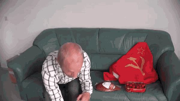 a man sits on a green couch with a red flag and a hammer and sickle