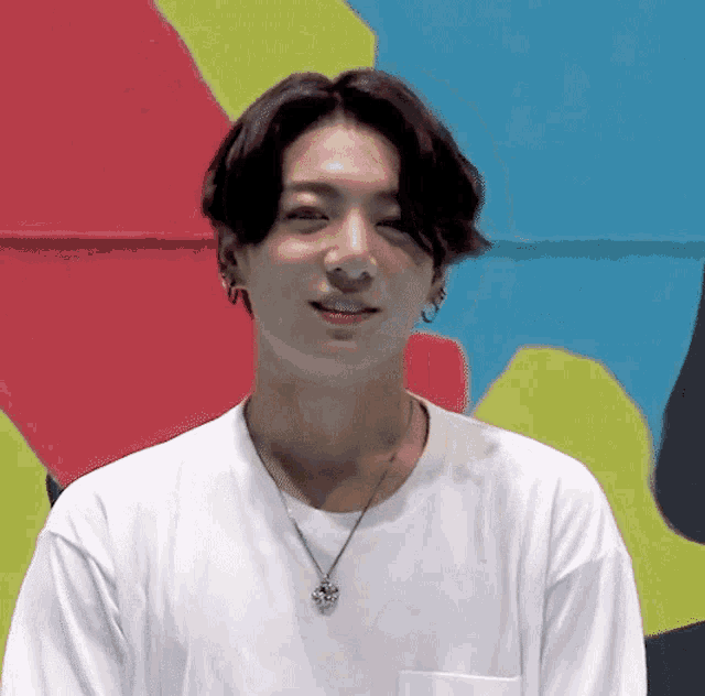 a young man wearing a white shirt and a necklace is smiling .