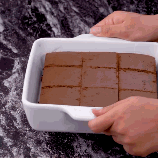 a person is holding a white casserole dish filled with chocolate