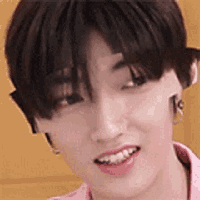 a close up of a person 's face with a pink shirt on and earrings .