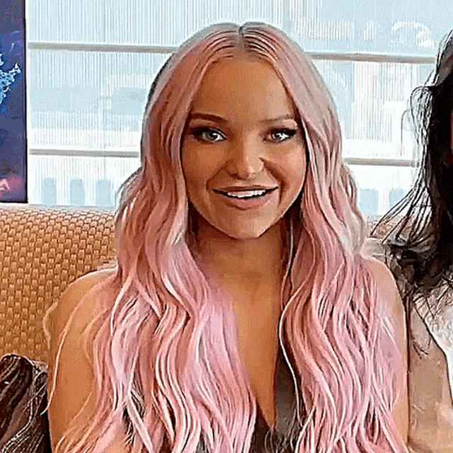 a woman with long pink hair is smiling and sitting on a couch .