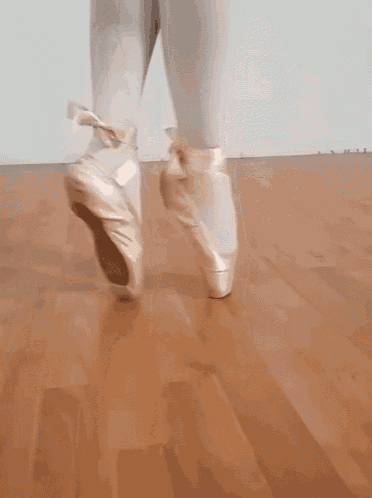 a close up of a person wearing pointe shoes on a wood floor