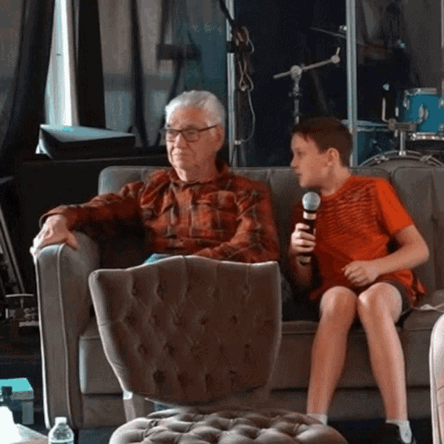 an elderly man and a young boy sit on a couch with a microphone