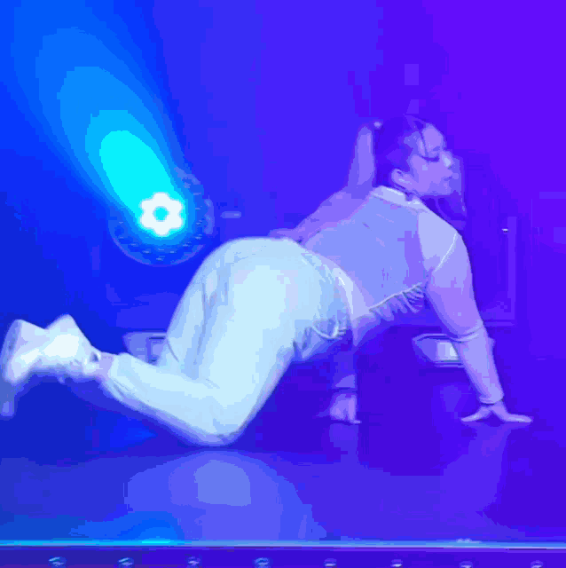 a woman is on her knees on a stage with a blue light behind her