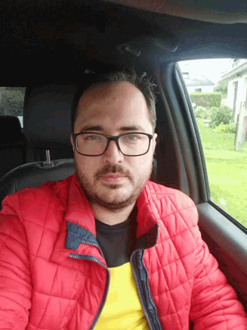 a man wearing glasses and a red jacket is in a car