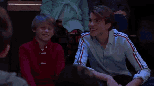 two young boys are sitting next to each other and smiling while watching a show .