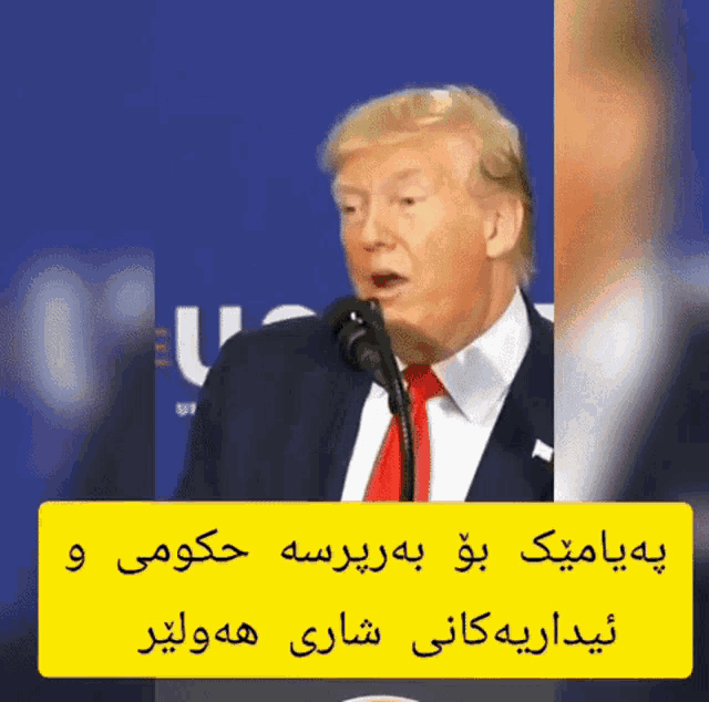 a man in a suit and tie is speaking into a microphone with arabic writing behind him
