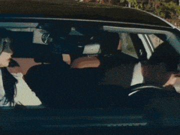 a man in a suit and tie stands next to a car