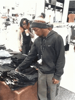 a man wearing a nike hoodie looks at a stack of black shirts