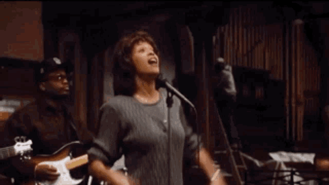 a woman singing into a microphone while a man plays a guitar in the background
