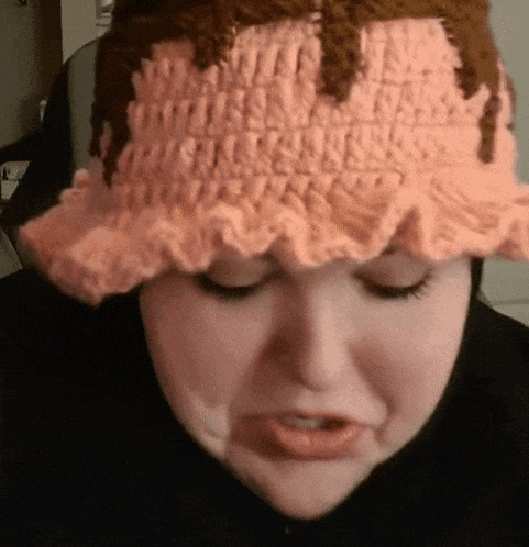 a woman wearing a pink crocheted hat making a face