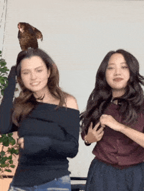 two women are standing next to each other with a bird on their head