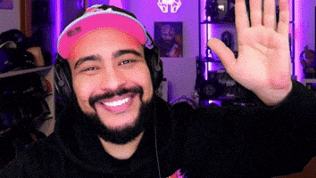 a man with a beard wearing headphones and a pink hat is smiling and waving .