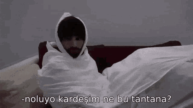 a man wrapped in a white blanket is sitting on a couch with a hood on .