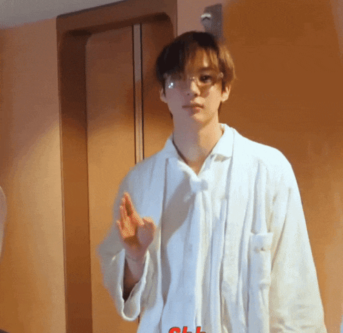a young man wearing glasses and a white shirt stands in front of a door