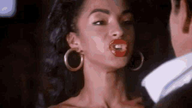 a woman with red lips and hoop earrings is looking at a man in a suit .