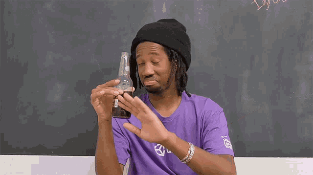 a man in a purple shirt is holding a bottle of beer