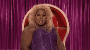 a drag queen in a purple dress is pointing at herself