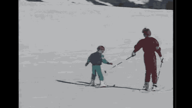 two people skiing down a snow covered slope with one wearing a blue vest
